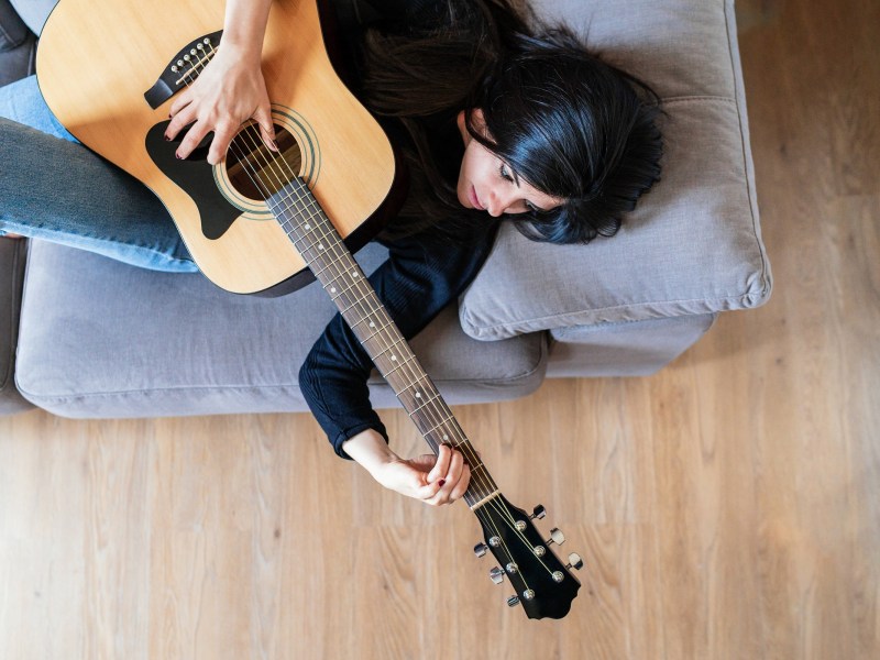 Frau liegt auf der Couch und spielt Gitarre