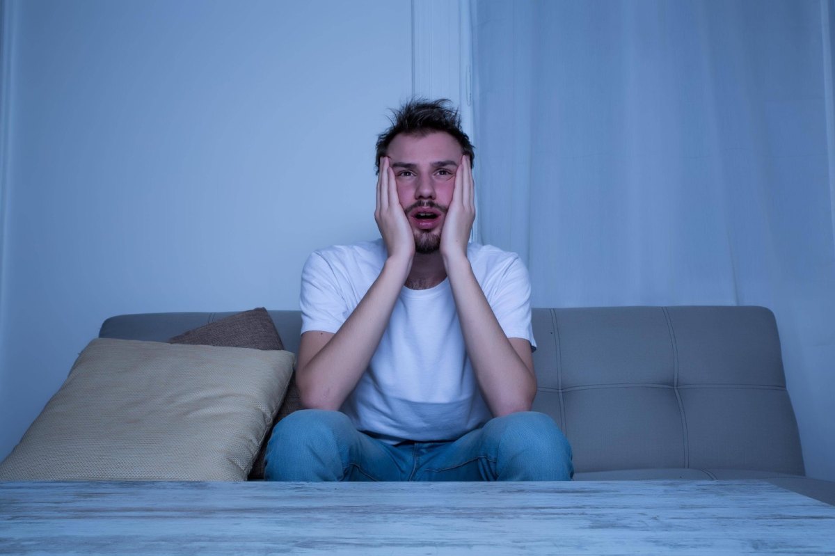 Mann sitzt auf dem Bett und guckt schockiert.