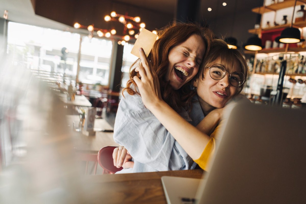 Zwei Frauen umarmen sich freudig vor einem Laptop.