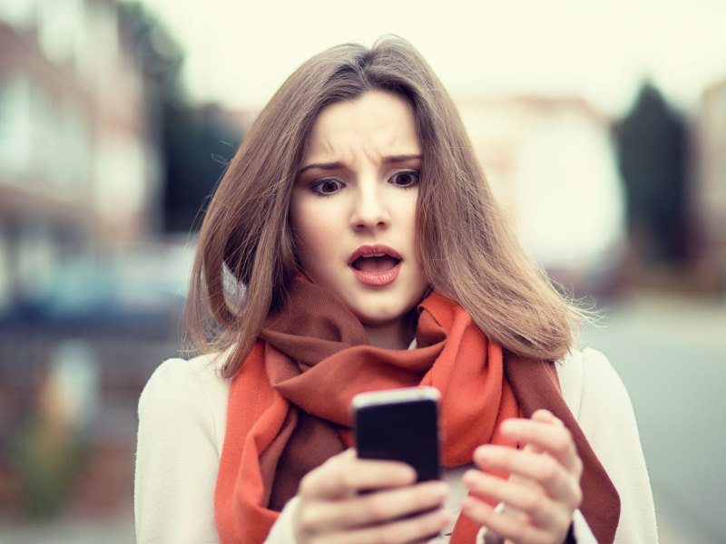 Frau guckt schockiert auf ihr Handy.