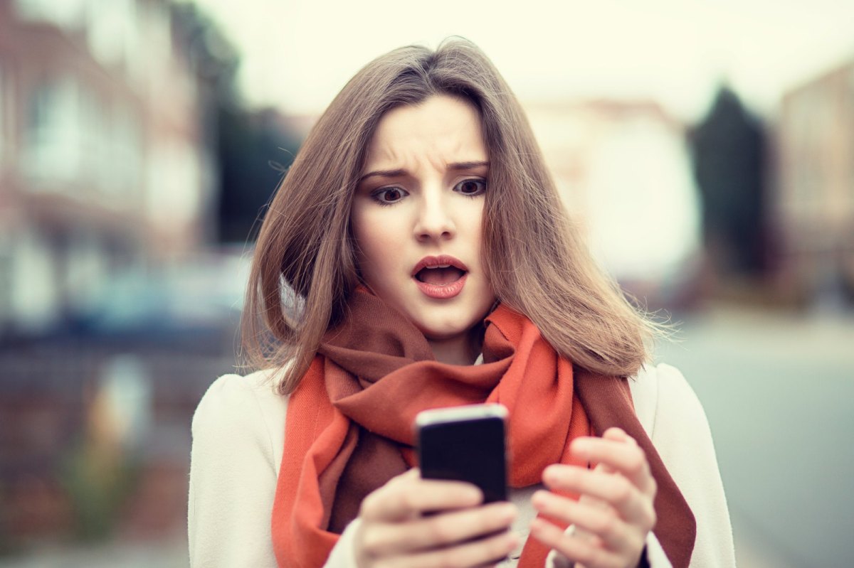 Frau guckt schockiert auf ihr Handy.