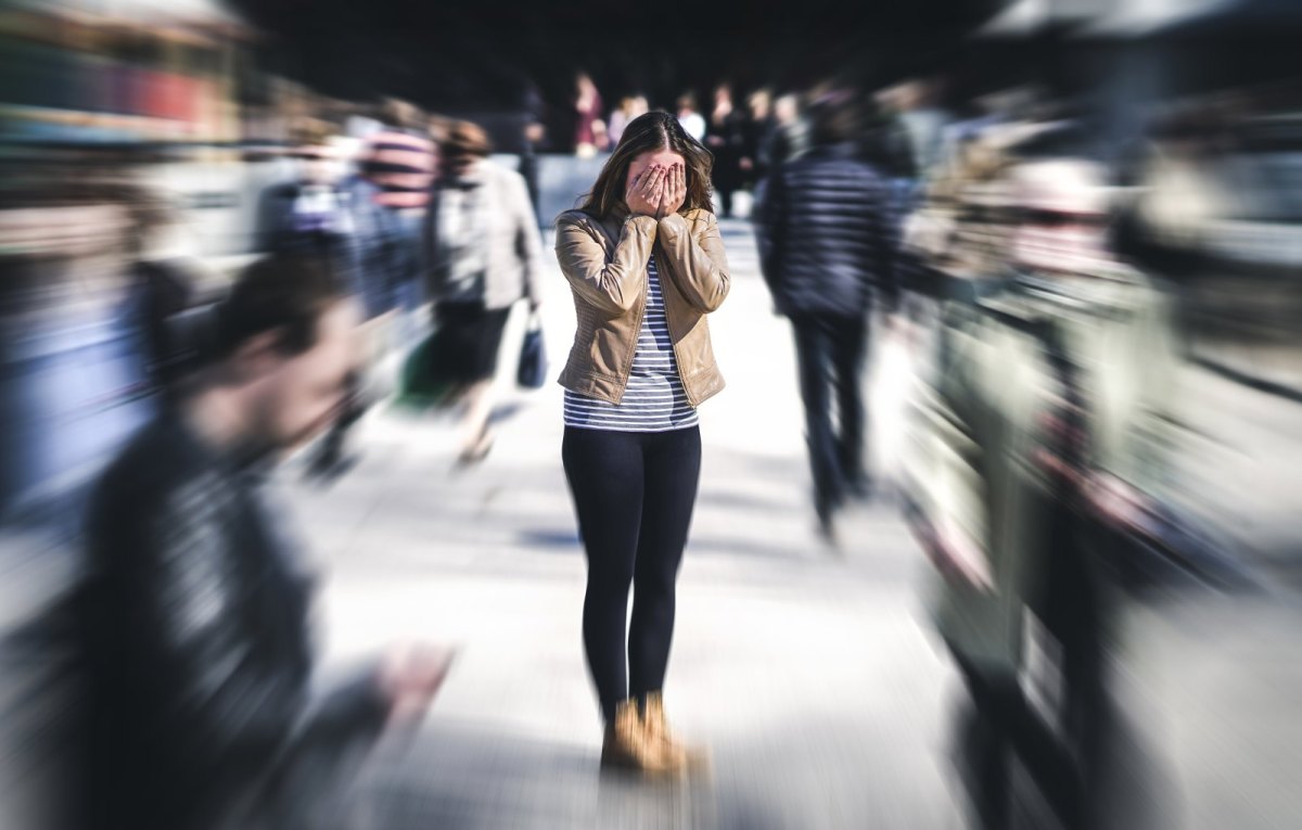 Frau steht mit Händen vor dem Gesicht in einer Menschenmenge.