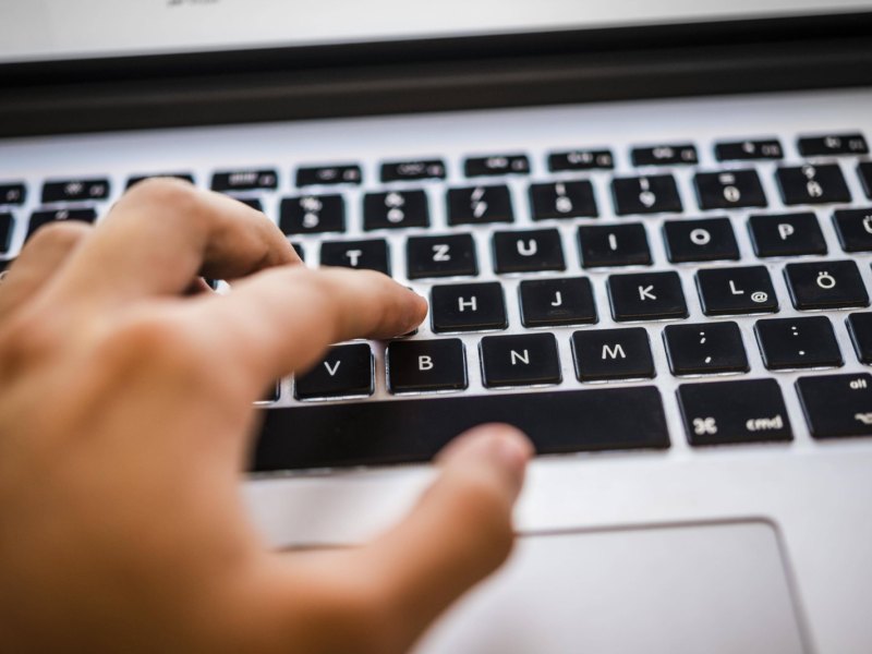 Eine Hand tippt auf der Tastatur eines Mac Books.