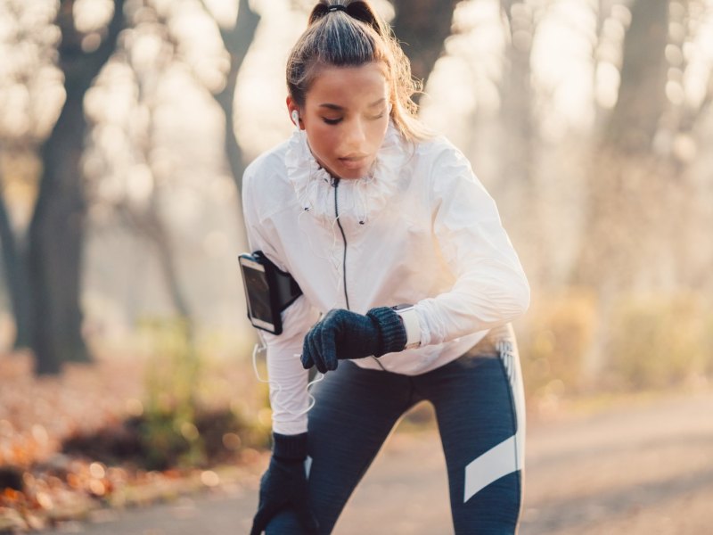 Frau schaut beim Joggen durch den Wald auf Fitness-Armband.