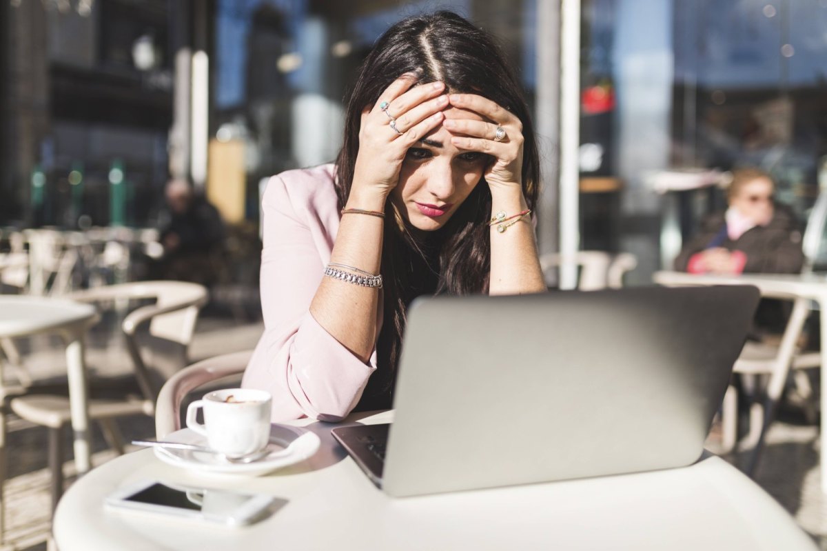 Frau sitzt geschockt vor ihrem Laptop im Café.