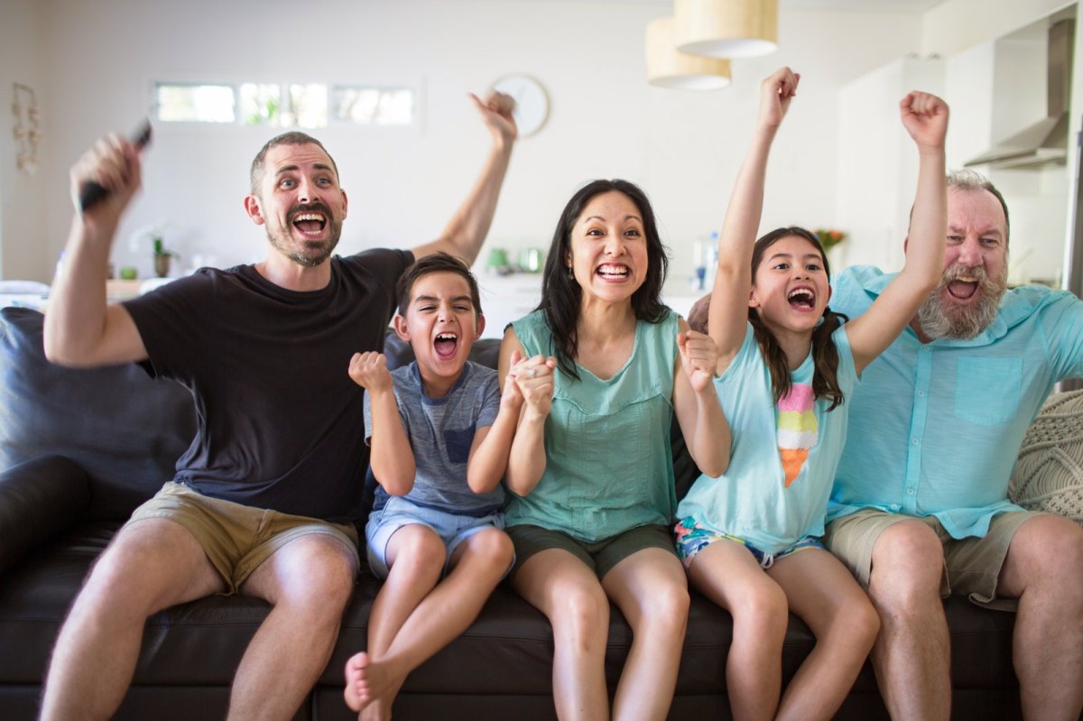 Familie sitzt auf dem Sofa und jubelt beim Fernsehen.