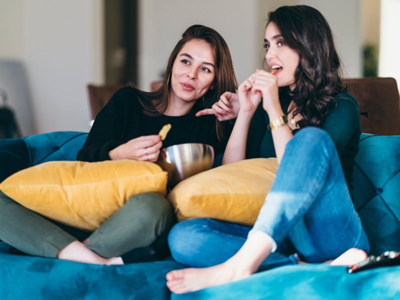 Zwei Frauen sitzen mit Chips vor dem Fernseher.