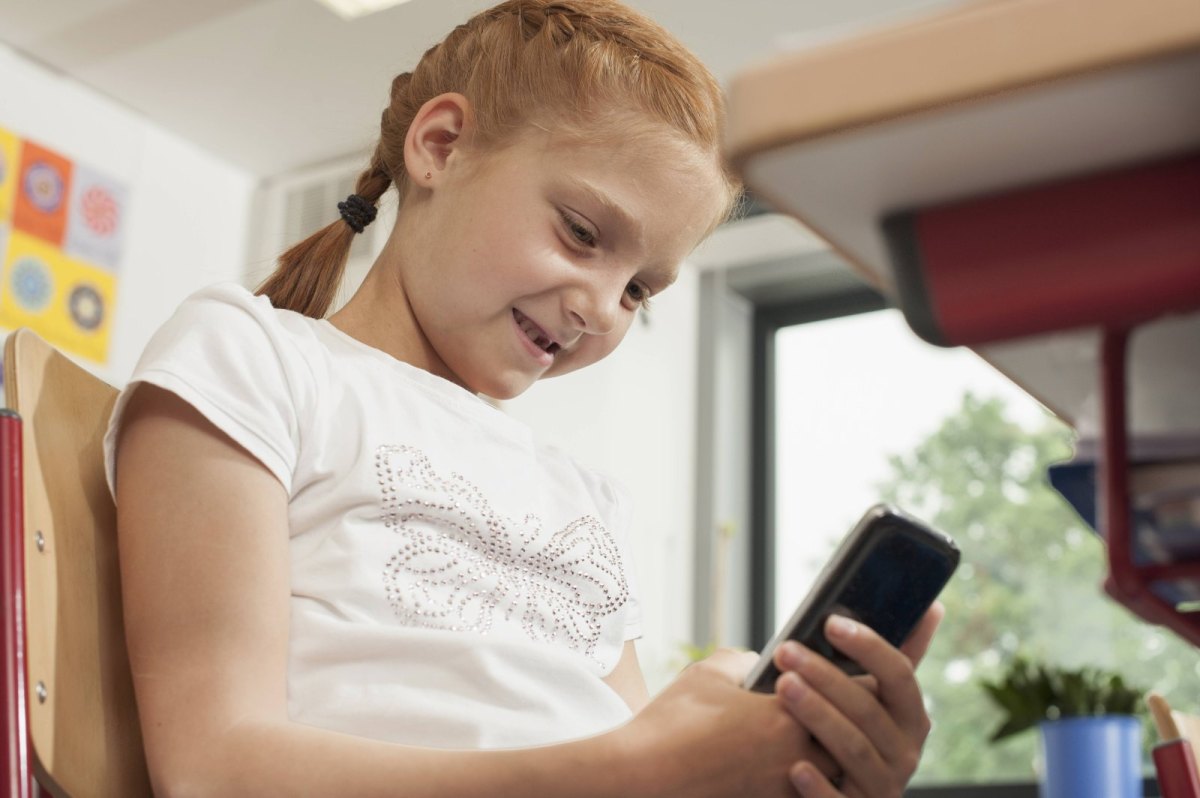 Grundschülerin schaut im Klassenraum auf ihr Smartphone