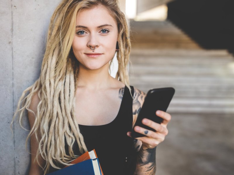 Junge Frau in einem Universitätsgebäude mit Büchern und Handy.