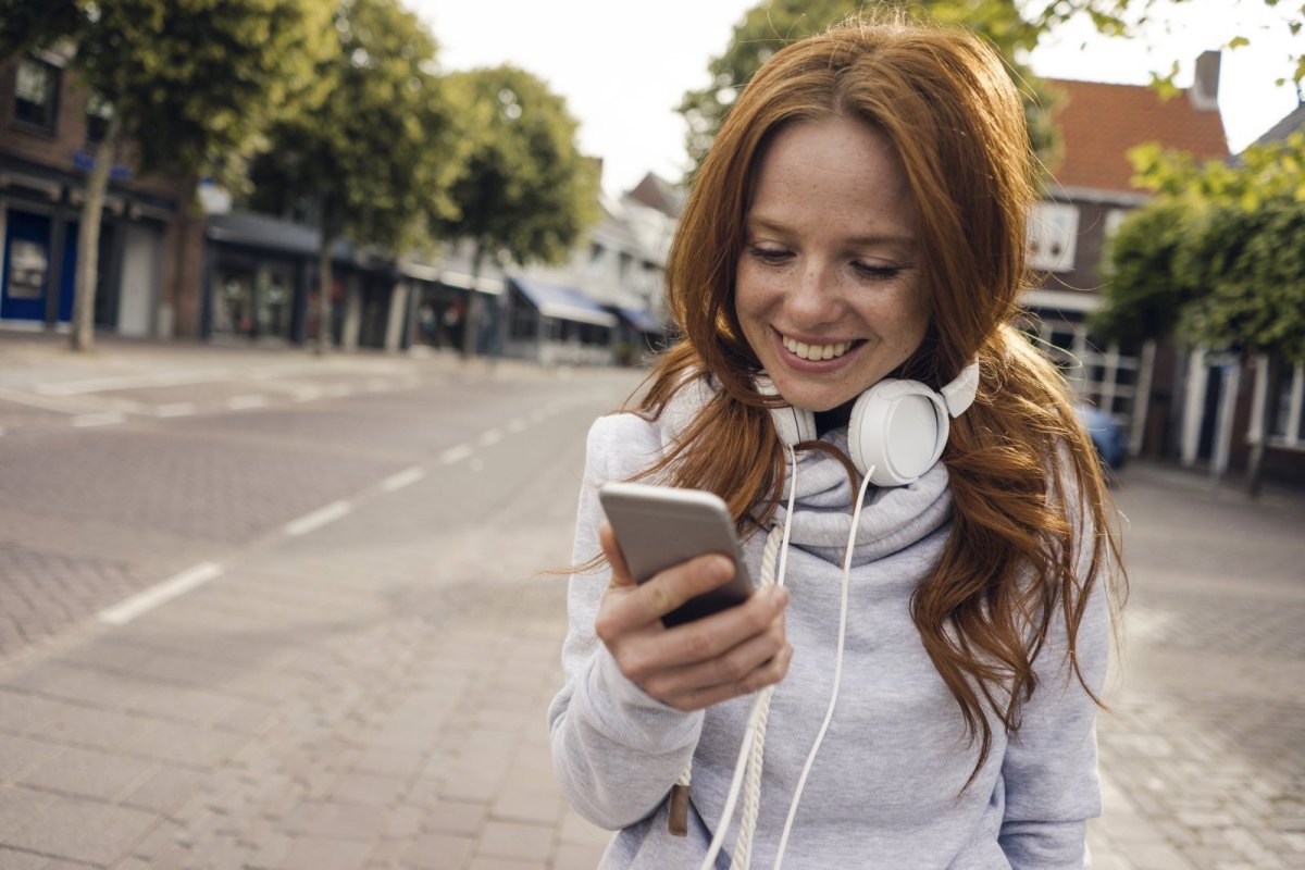 Eine Frau steht in der Stadt und schaut auf ihr Smartphone.