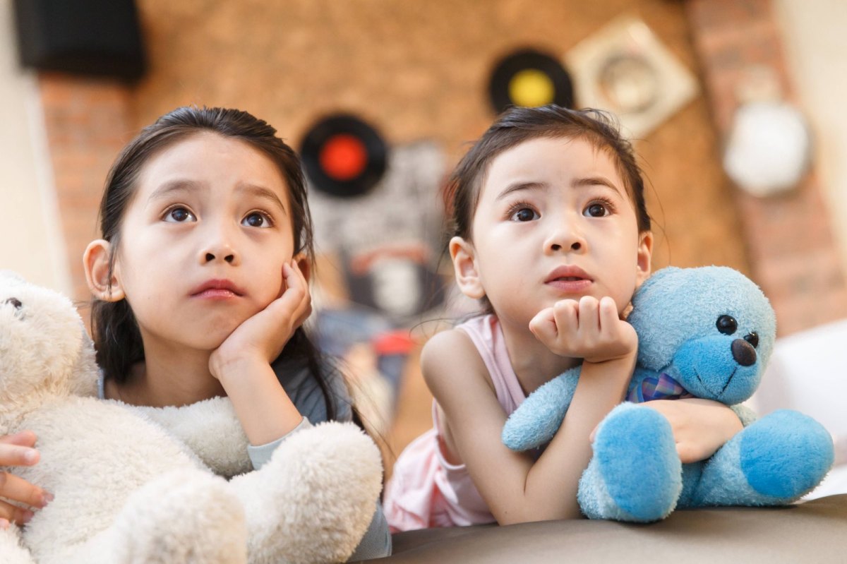 Zwei Kinder liegen auf dem Bett und gucken Fernsehen.