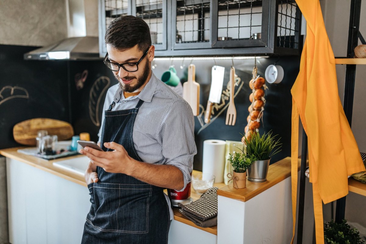 Mann steht mit Handy in der Küche.