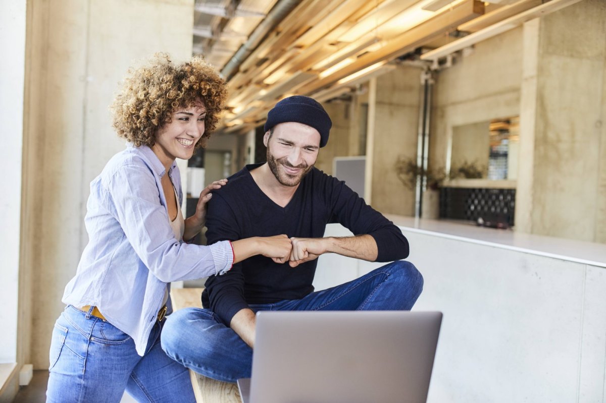 Mann und Frau geben sich eine Fistbump mit Laptop.