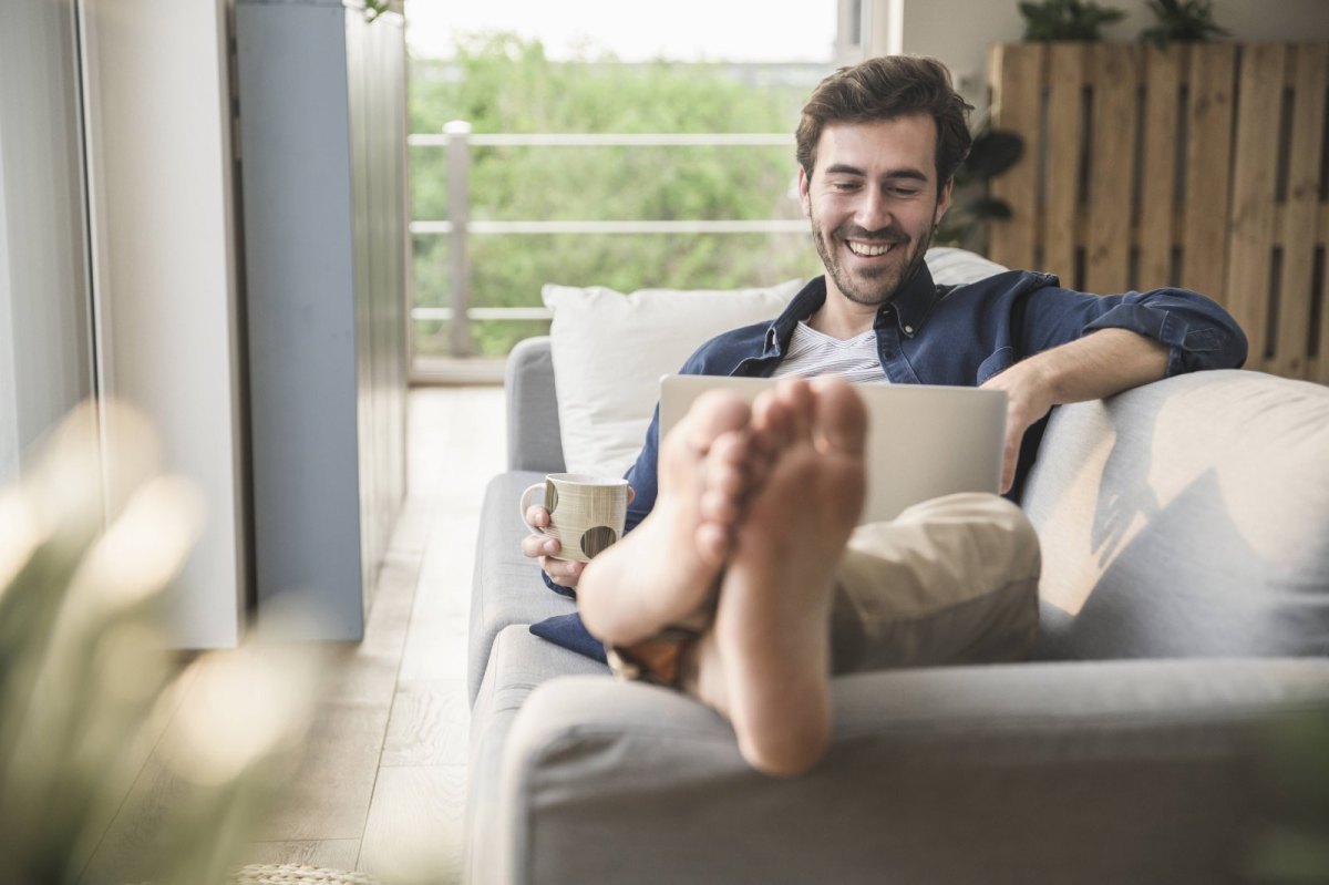 Mann mit Laptop auf Sofa.