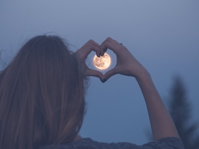 Frau umrahmt den Mond mit einem Herz