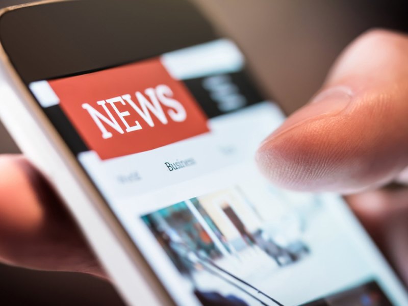 Smartphone mit geöffneter News-App in einer Hand