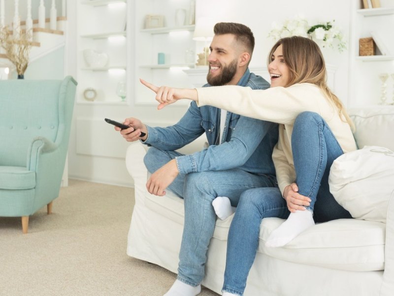 Pärchen sitzt freudig auf dem Sofa und schaut fernsehen.