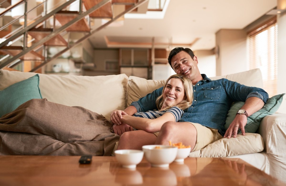 Mann und Frau liegen auf dem Sofa und schauen Fernsehen.