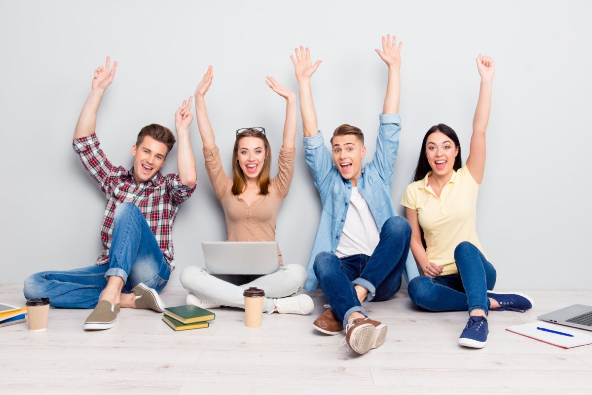 Vier Studenten arbeiten an ihren Laptops und freuen sich.