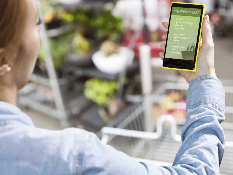 Eine Frau schaut im Supermarkt auf ihr Smartphone.