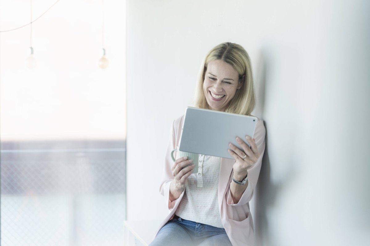 Frau lacht mit Tablet in der Hand.