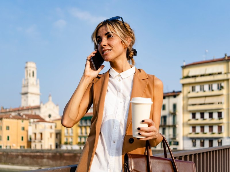 Frau telefoniert mit Kaffeebecher in der Hand.