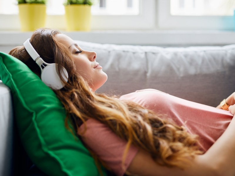 frau liegt mit Kopfhörern auf dem Sofa.