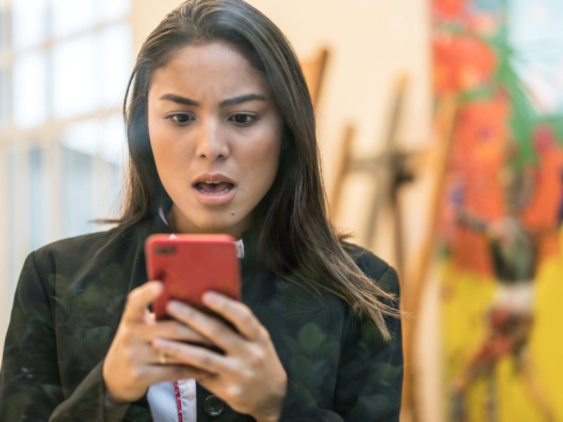 Frau sieht schockiert auf ihr Handy.