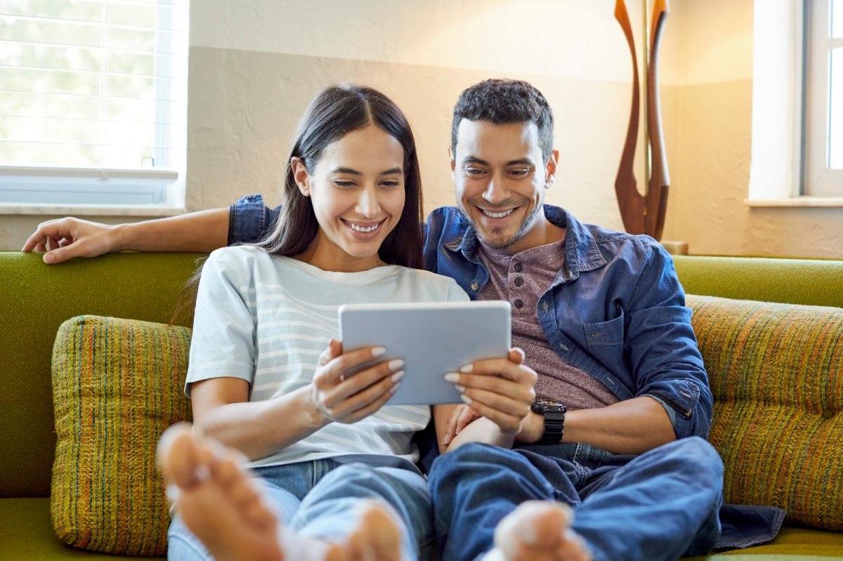 Ein Pärchen auf dem Sofa blickt auf ein Tablet.