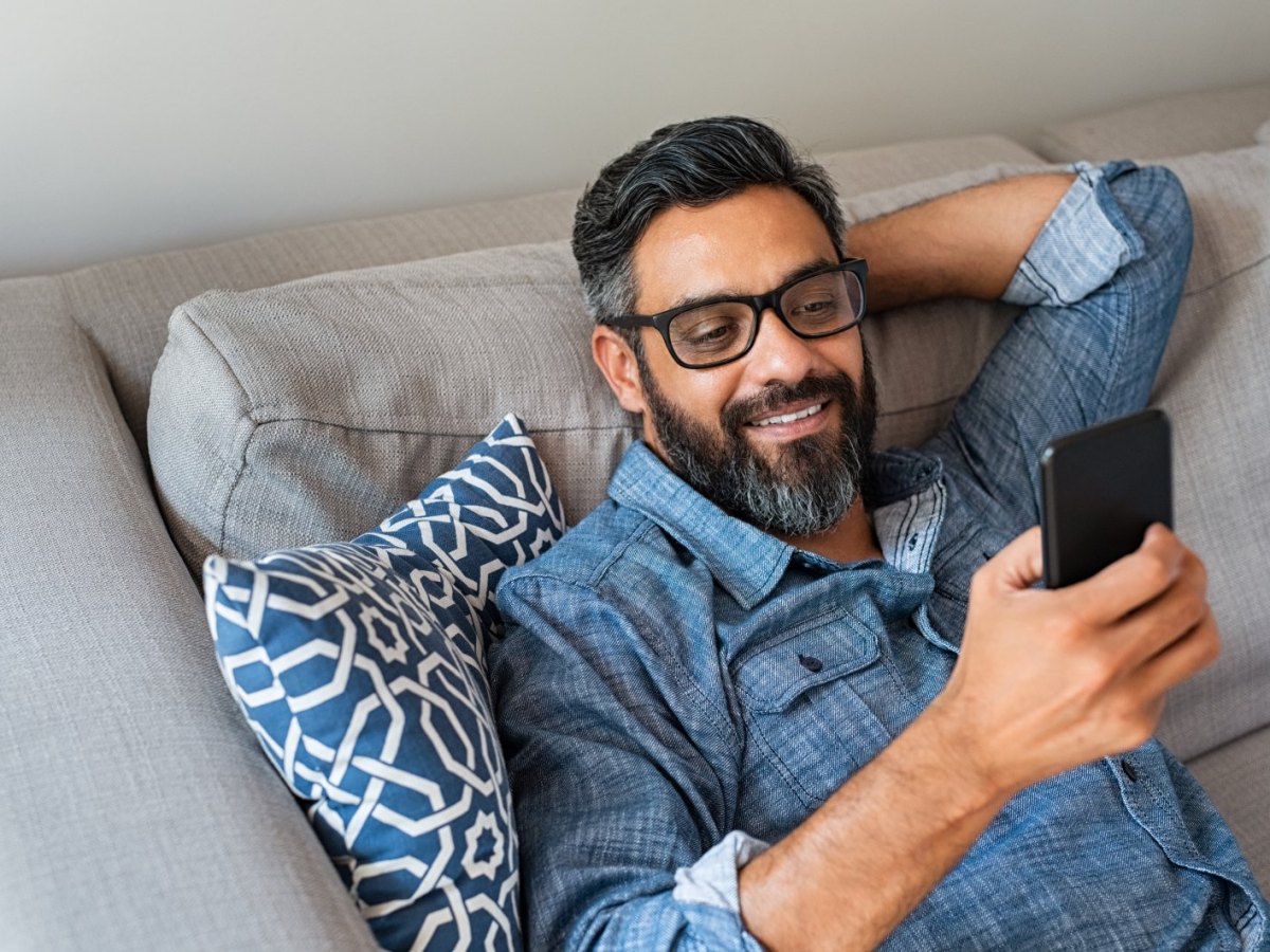 Mann auf dem Sofa blickt auf sein Handy.