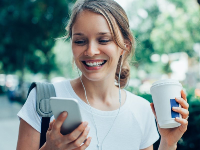 Frau mit Kopfhörern schaut aufs Handy.