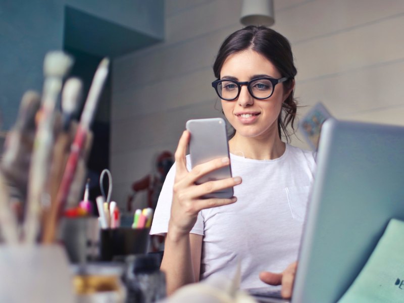 Frau sitzt am Schreibtisch und schaut auf ihr Handy.