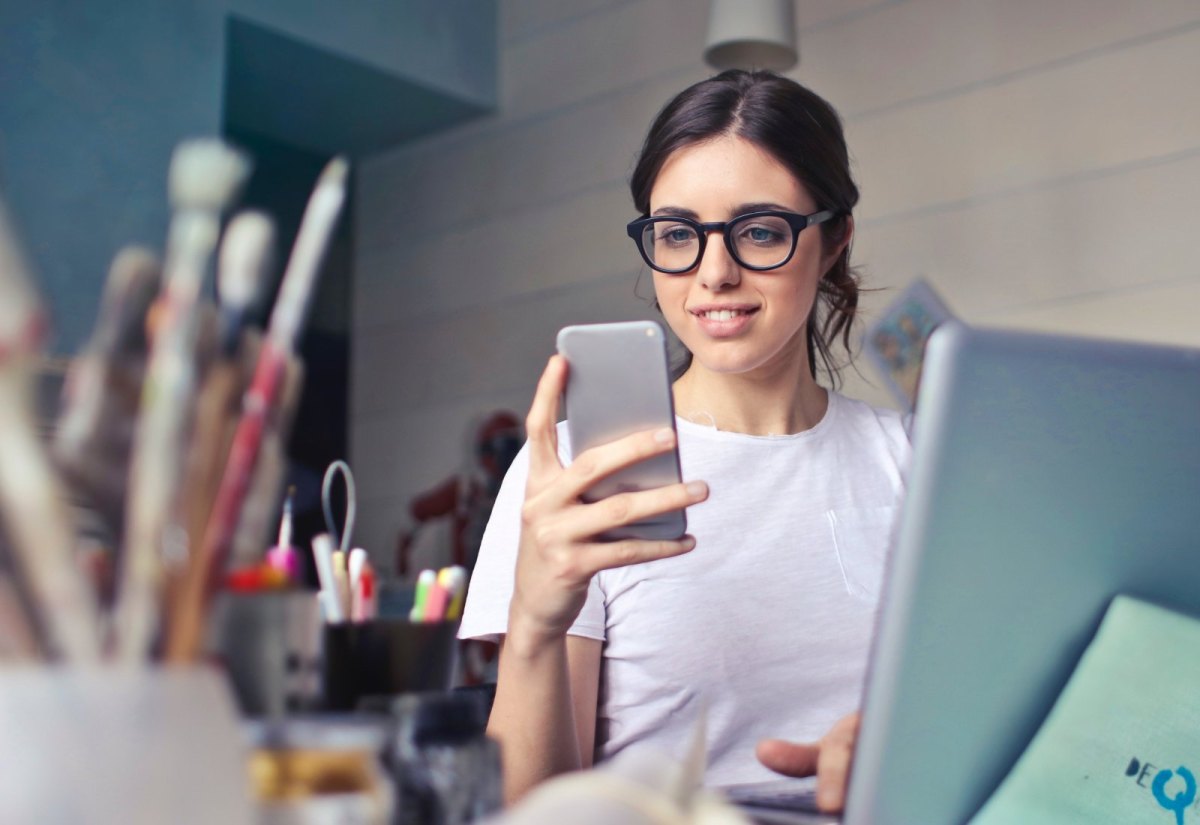 Frau sitzt am Schreibtisch und schaut auf ihr Handy.