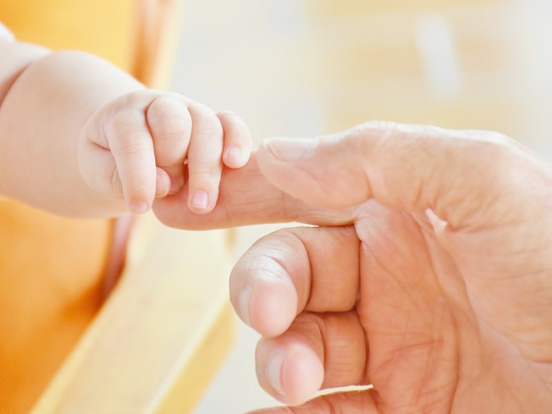 Hand eines Erwachsenen greift Fuß eines Babys.