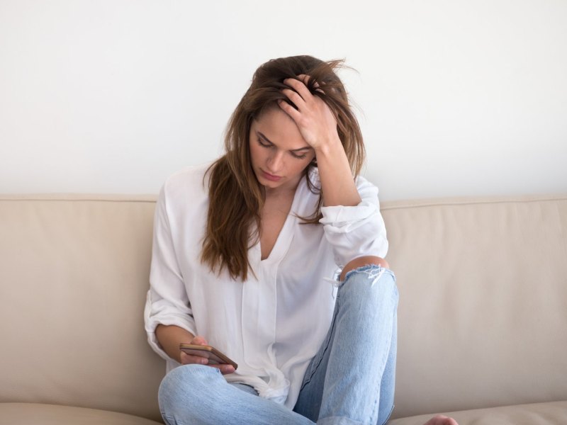 Frau mit Handy besorgt auf dem Sofa