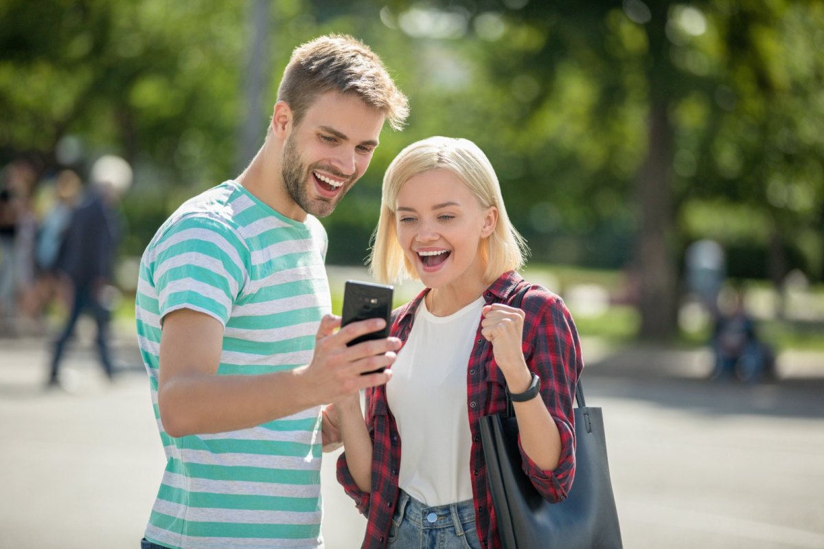 Ein Mann und eine Frau blicken auf ein Handy und freuen sich.