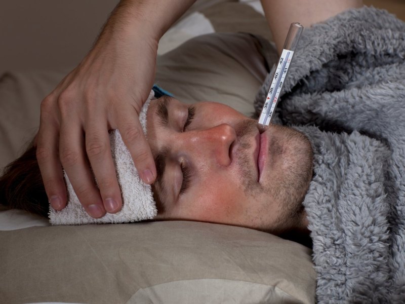 Mann mit Fiebertermometer im Mund.