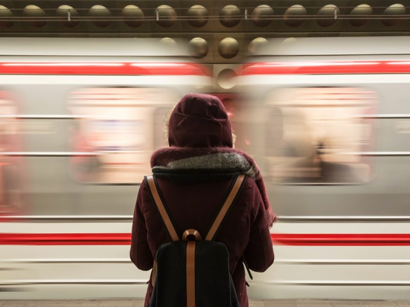 Eine junge Frau steht mit dem Rücken zum Betrachter am Bahnsteig