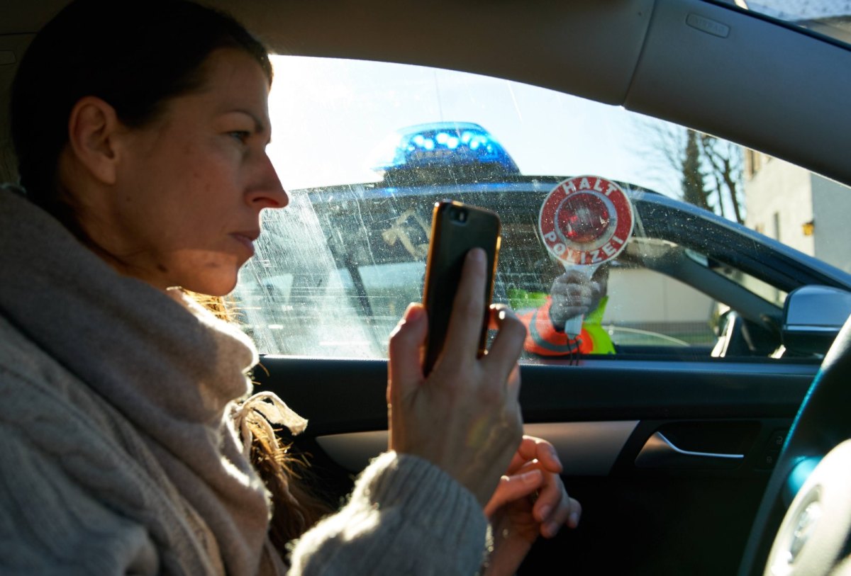 Eine Frau im Auto hält ein Smartphone in der Hand und wird von der Polizei angehalten.