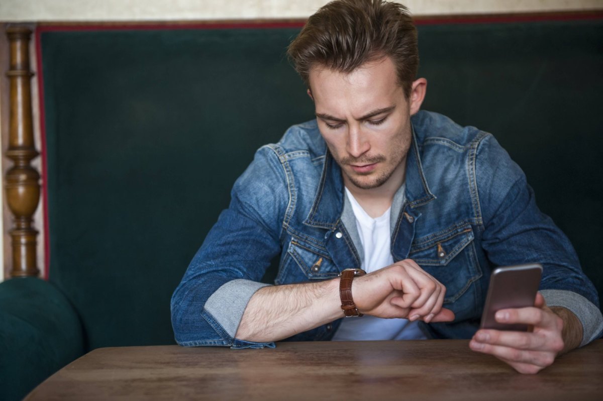 Mann ist am Handy und guckt auf seine Armbanduhr.