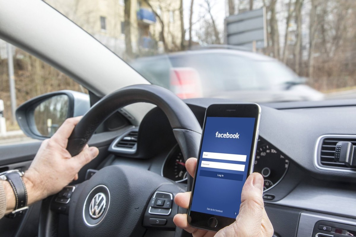 Mann im Auto mit Facebook auf dem handy
