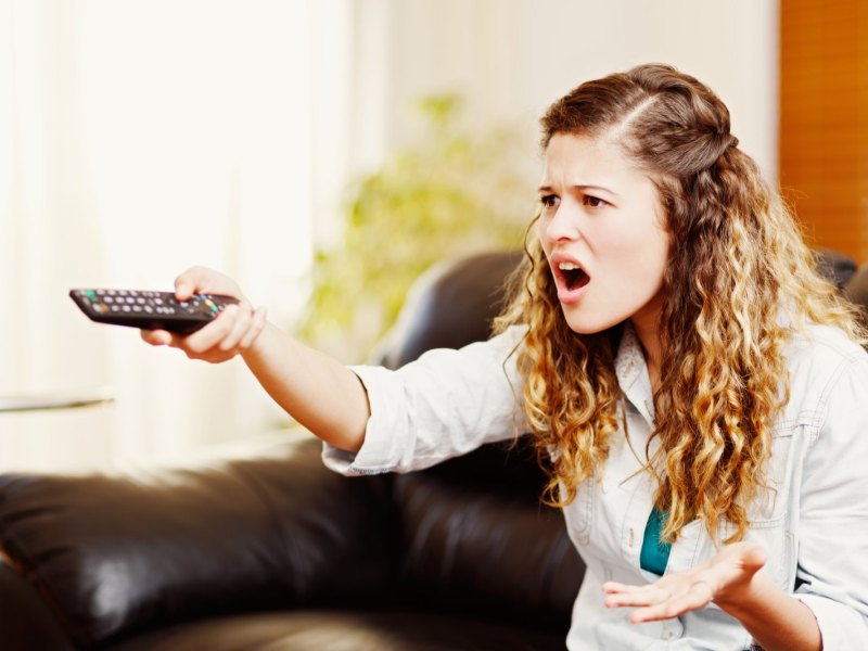 Frau sitzt genervt vor dem Fernseher.