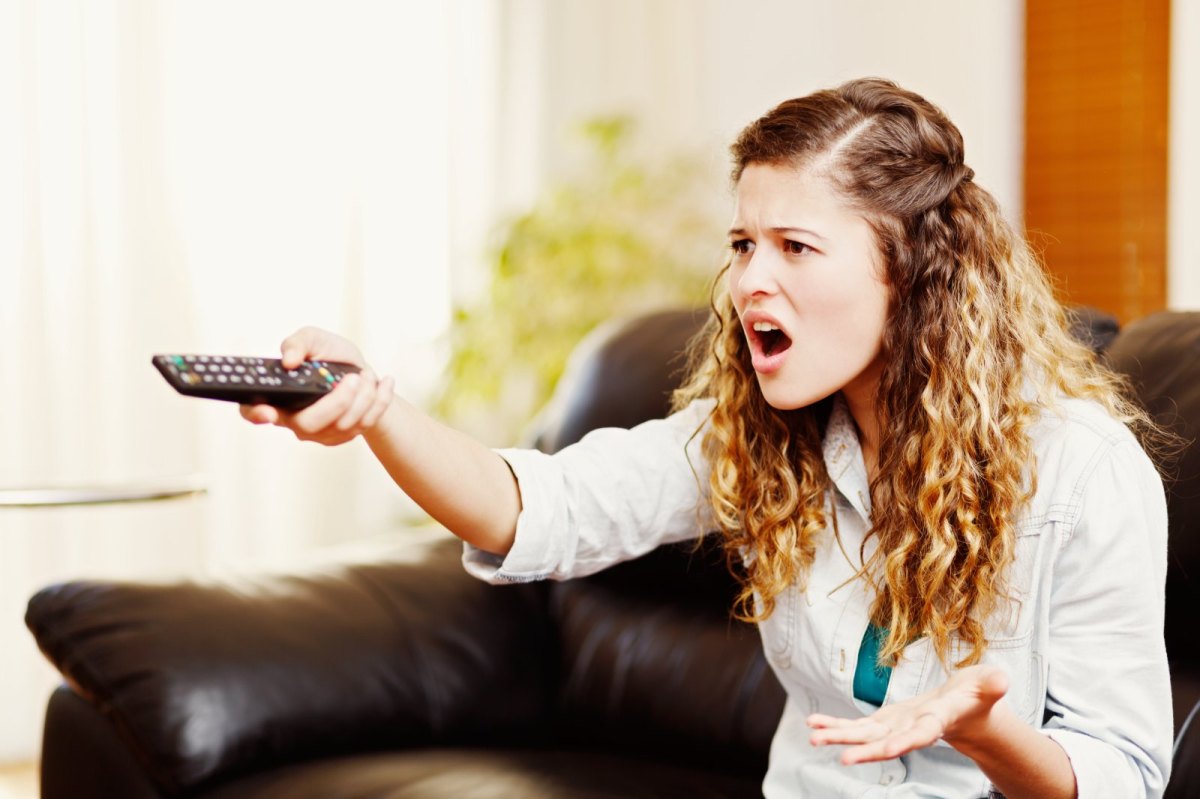 Frau sitzt genervt vor dem Fernseher.