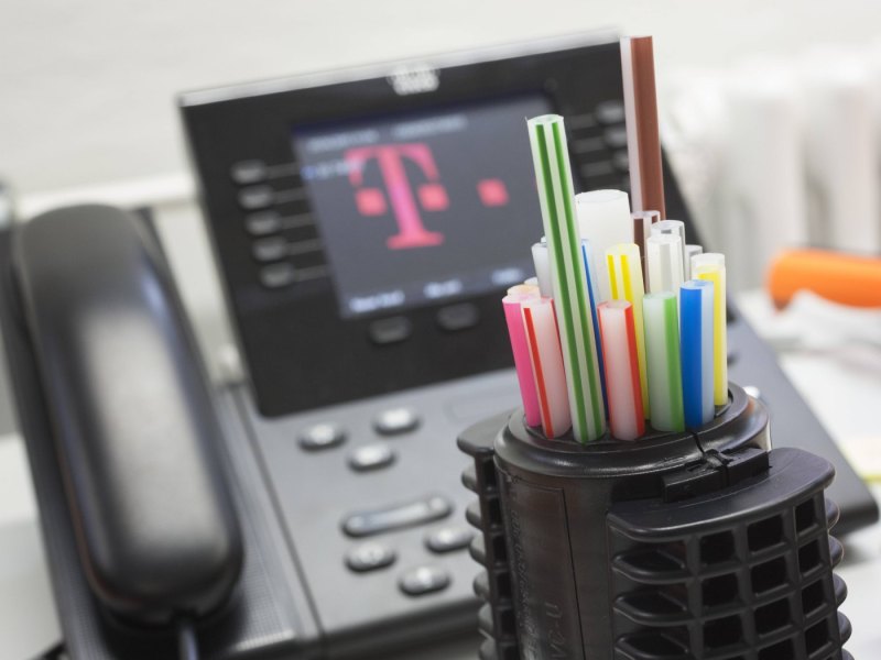 Leere Röhrchen für Glasfasern vor einem Telefon mit Telekom-Symbol auf dem Display