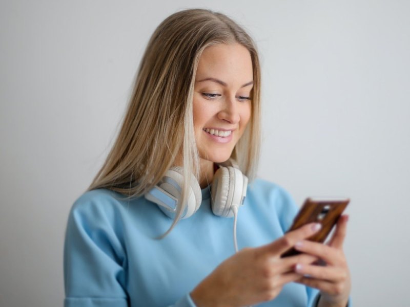 Eine Frau schaut auf ihr Handy und hat Over-Ear-Kopfhörer um ihren Hals gelegt.