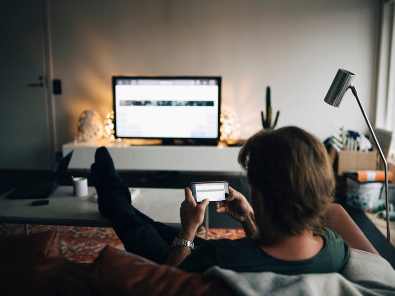 Mann sitzt mit Handy vor dem Fernseher