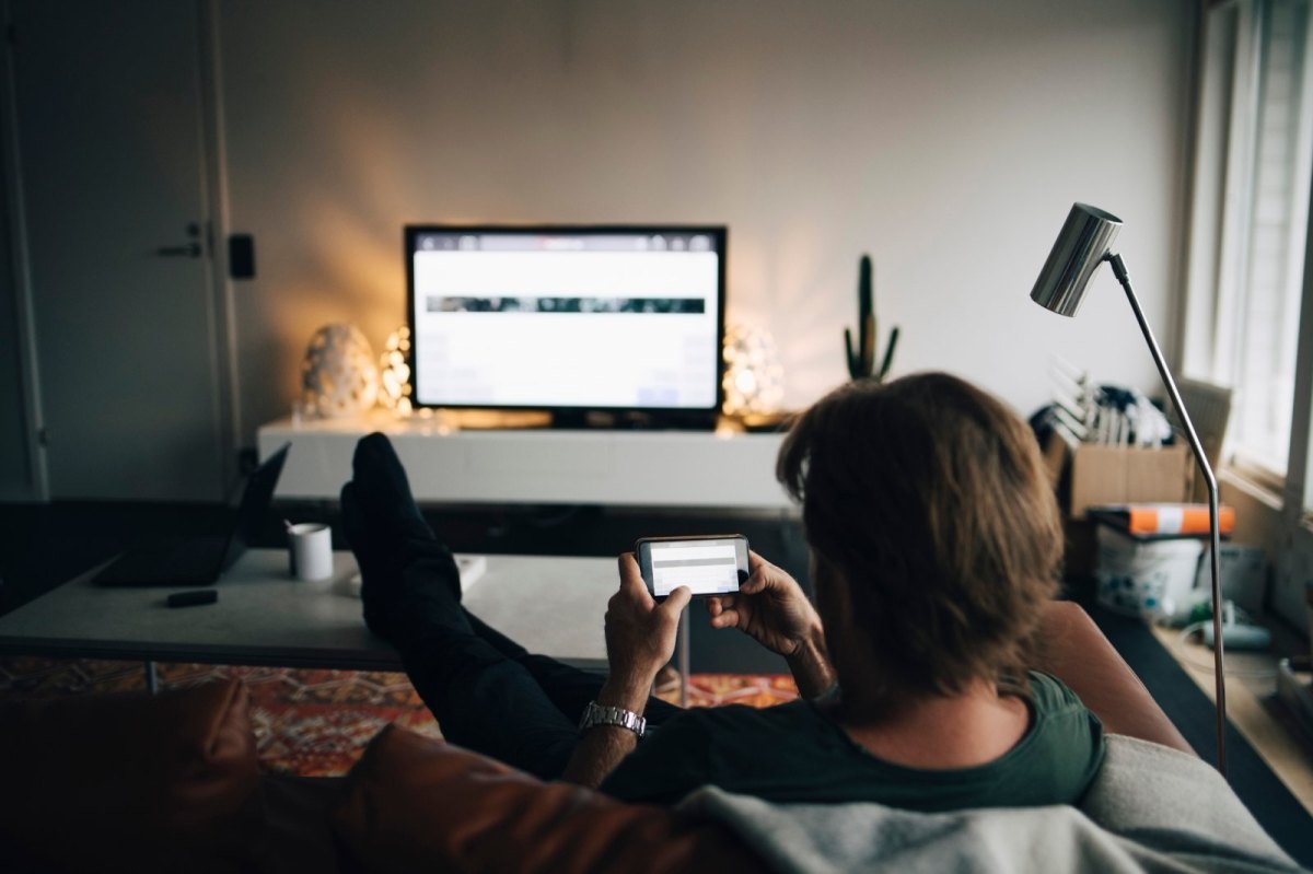 Mann sitzt mit Handy vor dem Fernseher