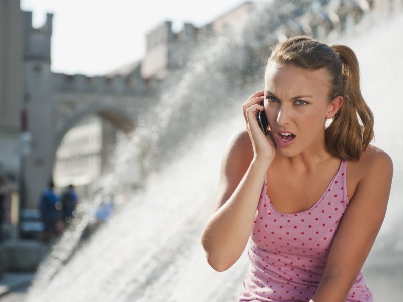 Frau hält verärgert ihr Handy ans Ohr.