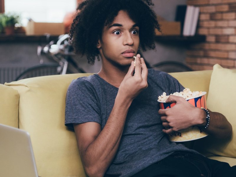 Mann sieht mit Popcorn in der Hand geschockt fern.