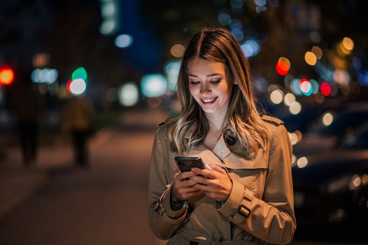 Frau schaut lächelnd auf ihr Handy.